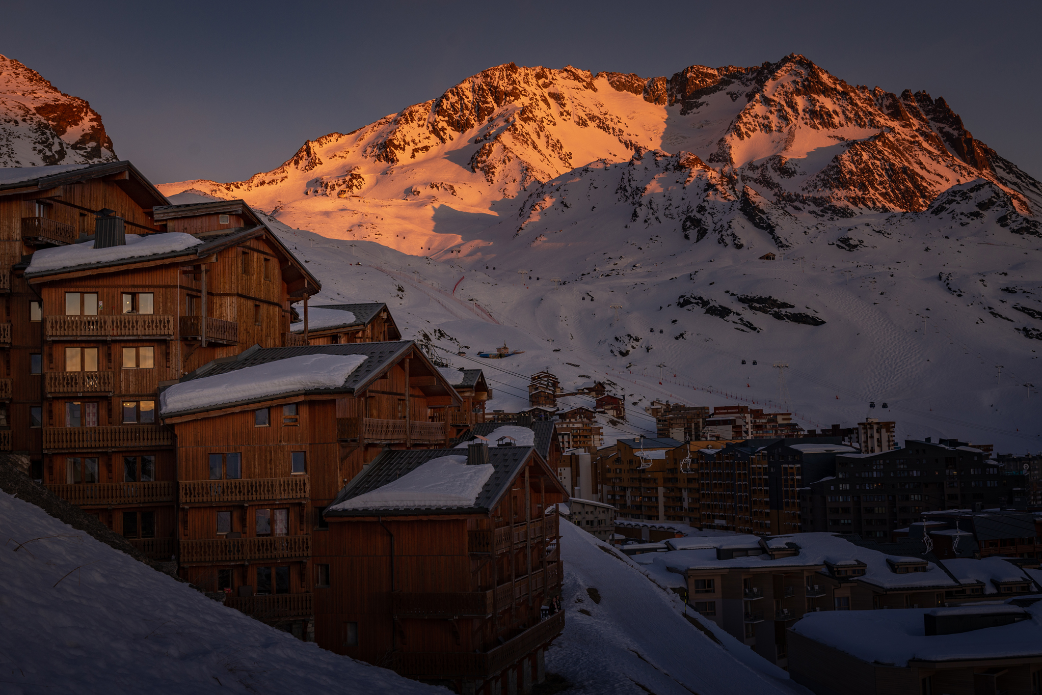 Zachód słońca nad Val Thorens: drewniane budynki Les Balcons i oświetlony szczyt